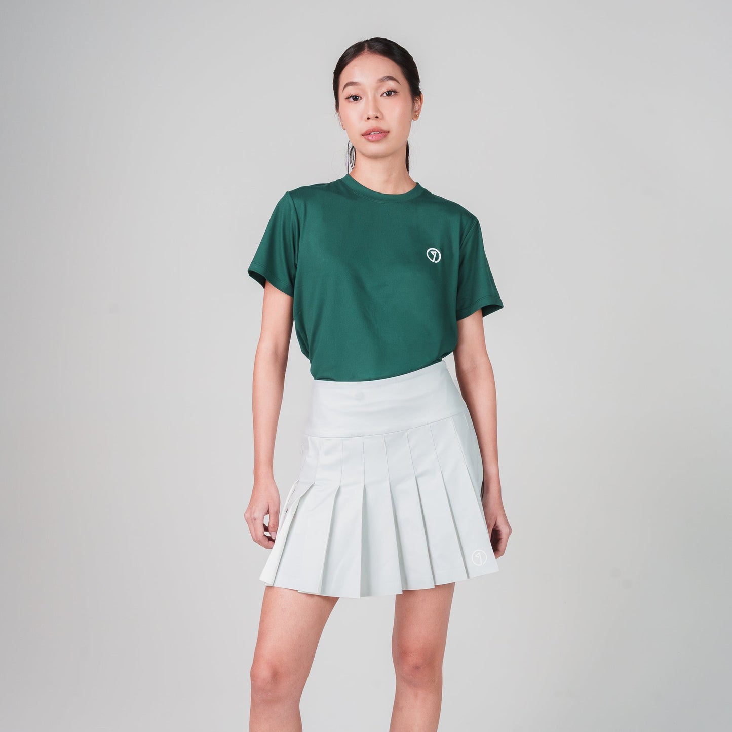 Person wearing a green t-shirt and white pleated skirt on a plain background