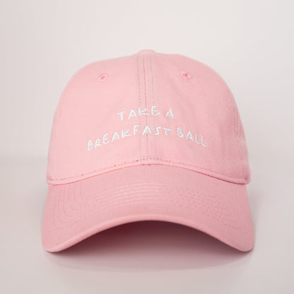 Pink cap with 'Take a Breakfast Ball' text on a light gray background