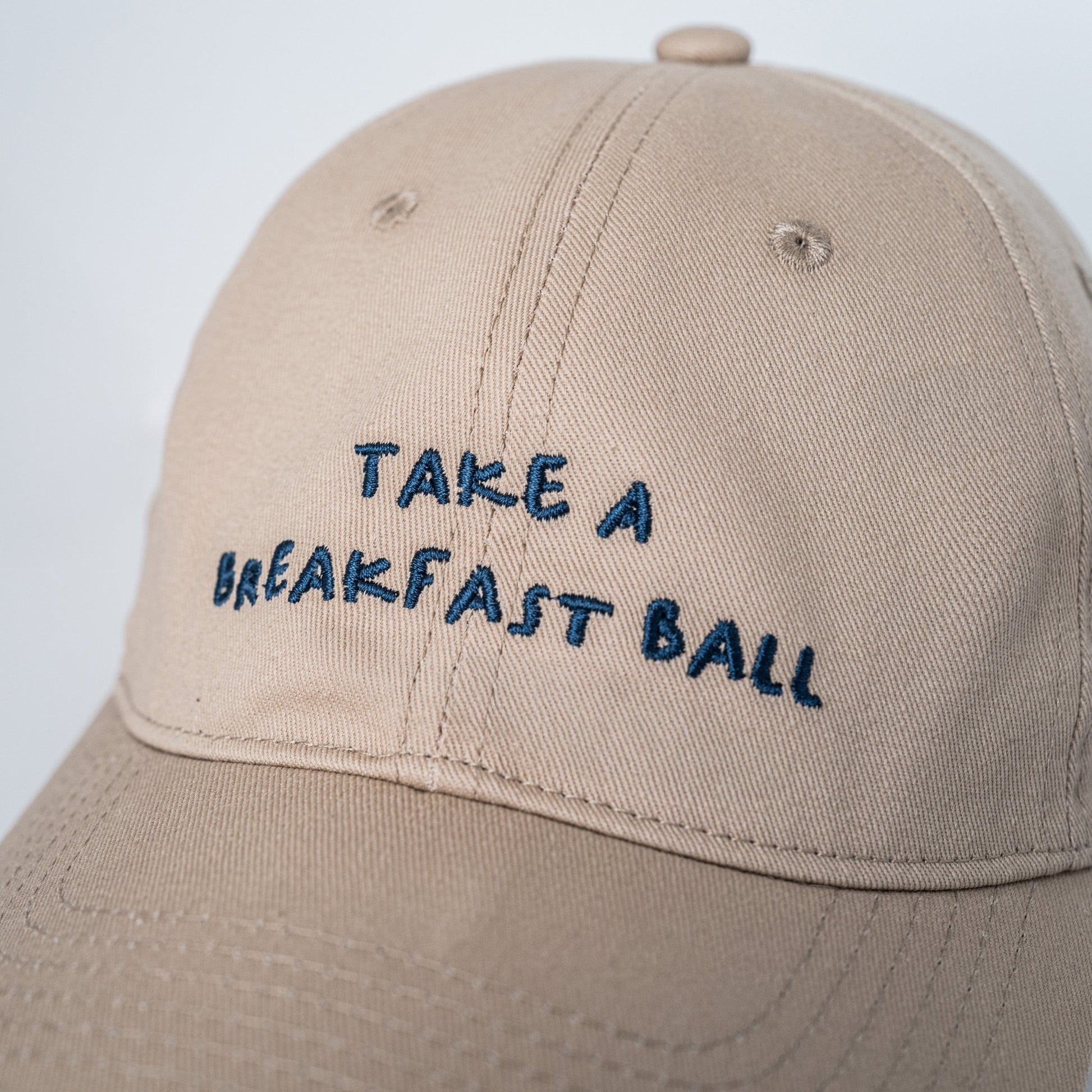 Beige cap with 'Take a Breakfast Ball' text on a light gray background