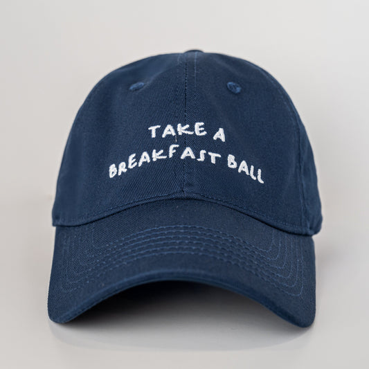 Navy blue cap with 'Take a Breakfast Ball' text on a light gray background