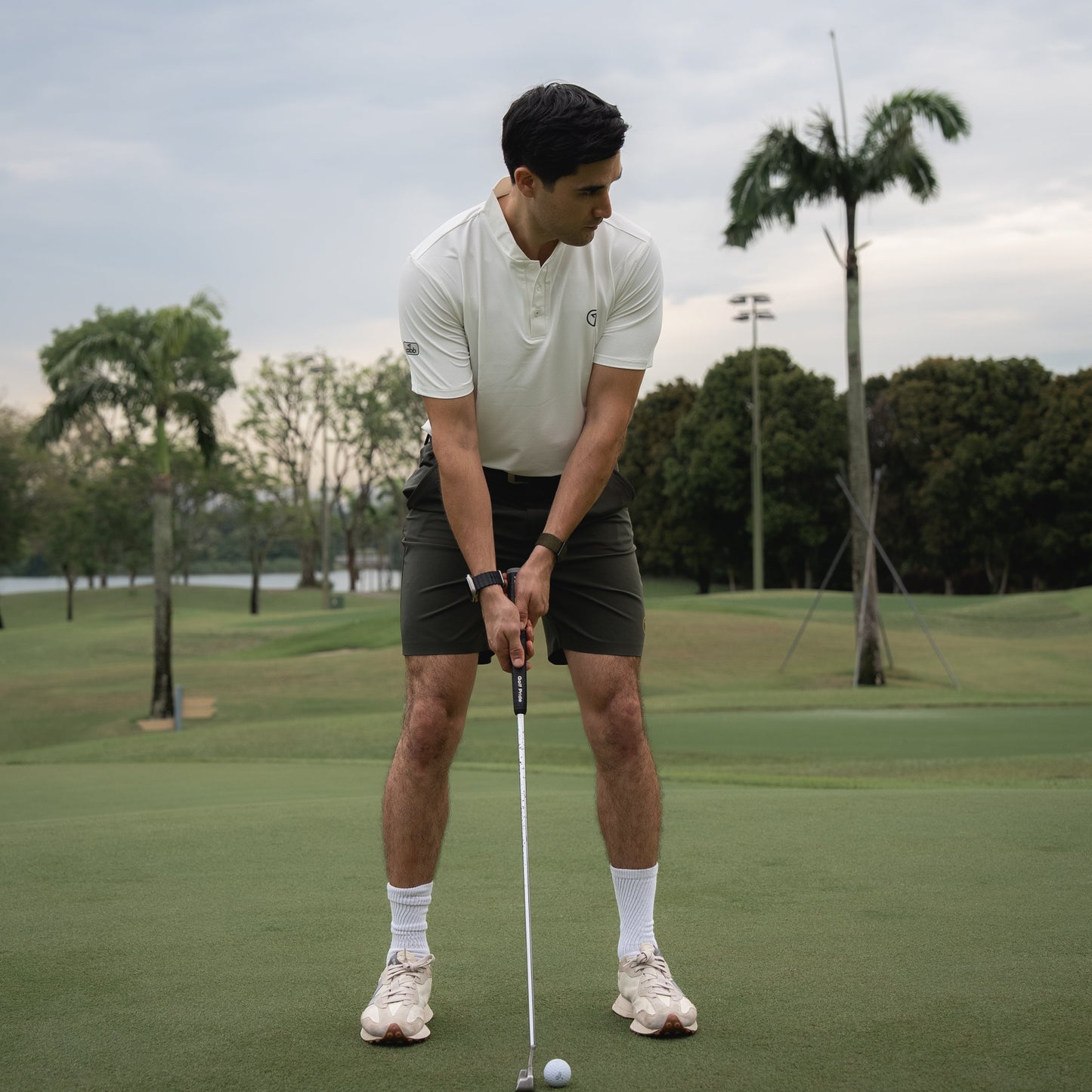 Man playing golf on a green course with trees and a cloudy sky in the background