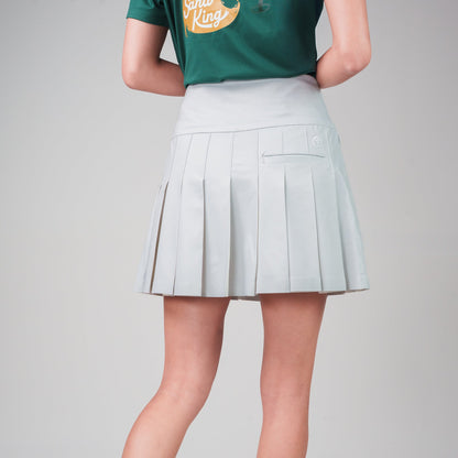 Person wearing a green shirt, light blue pleated skirt, and white sneakers on a gray background