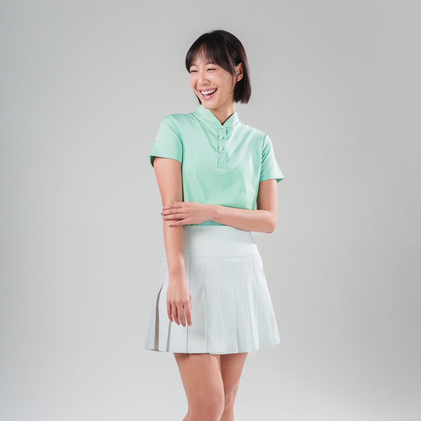 Woman wearing a light green polo shirt and white skirt on a gray background