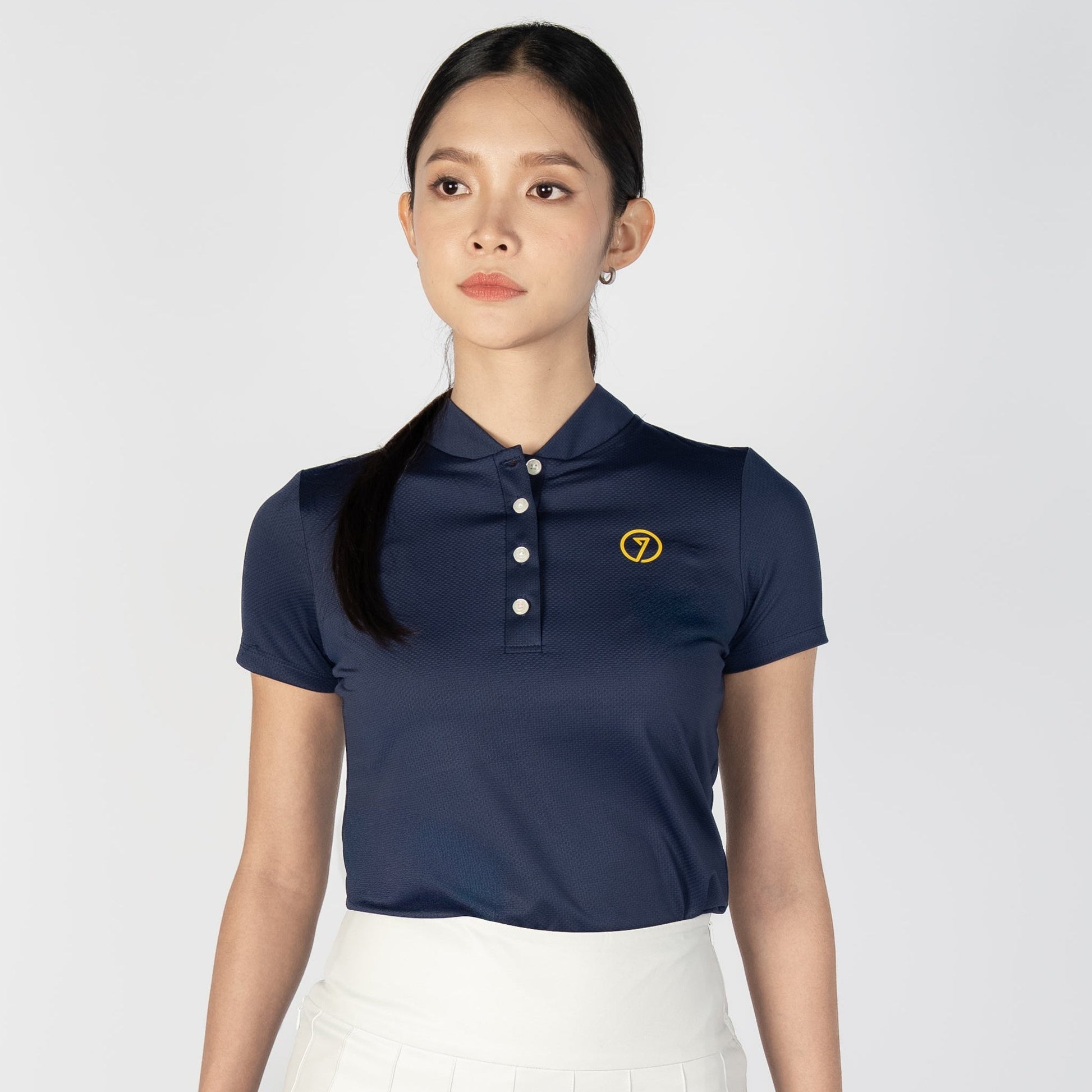 Woman wearing a navy blue polo shirt and white skirt holding a golf club on a white background